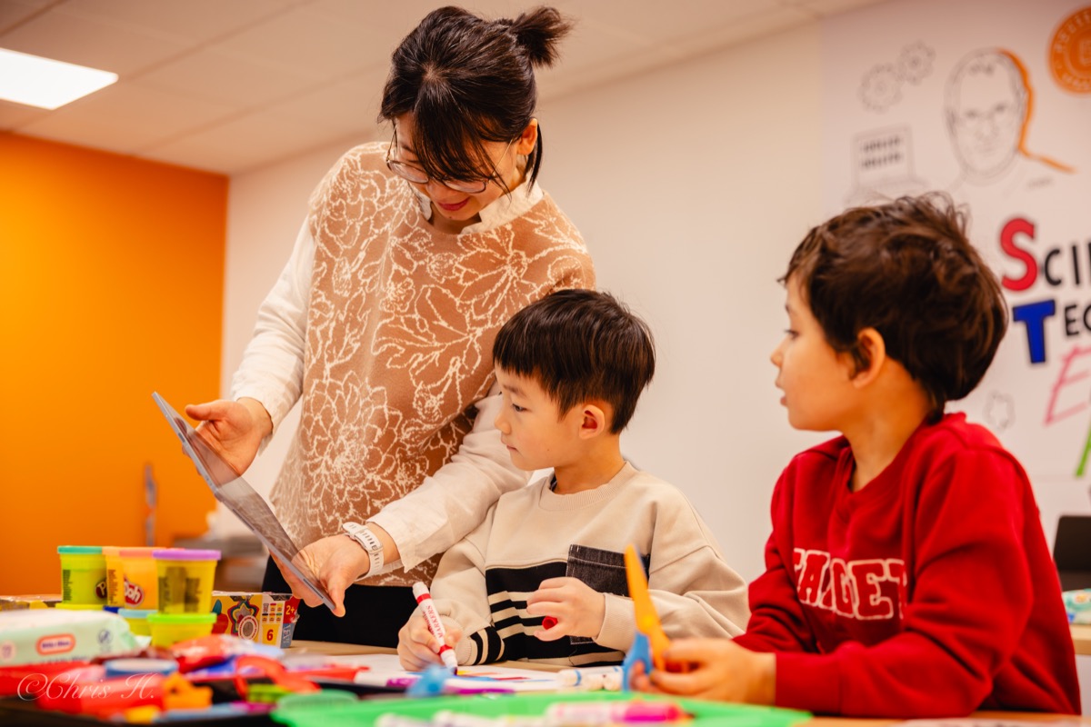 A KindleWood facilitator guiding two children through a hands-on creative project.